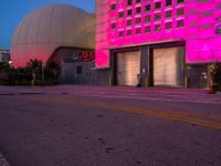 a fire hydrant sitting in the middle of a parking lot outside a building that has pink lighting on it