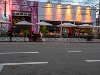 people sitting outside a pink restaurant with large umbrellas in the shade on a cloudy day