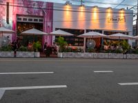 people sitting outside a pink restaurant with large umbrellas in the shade on a cloudy day