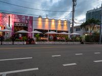 people sitting outside a pink restaurant with large umbrellas in the shade on a cloudy day