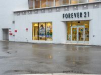 a shopfront with rain on the ground and sign above a store window that says forever 21