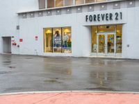 a shopfront with rain on the ground and sign above a store window that says forever 21