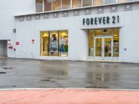 a shopfront with rain on the ground and sign above a store window that says forever 21