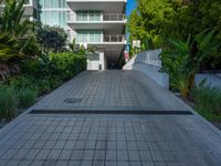the entrance to an apartment with palms trees and bushes in the foreground, next to a concrete driveway