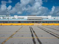 an empty parking lot filled with lots of buildings and trucks in the background of a cloudy blue sky