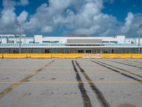 an empty parking lot filled with lots of buildings and trucks in the background of a cloudy blue sky