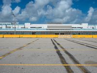 an empty parking lot filled with lots of buildings and trucks in the background of a cloudy blue sky