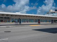 a bus station on a road with cars driving around it and a blue sky behind