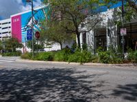 an empty street with a building on the side and traffic light next to it under some trees