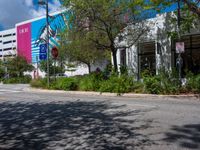 an empty street with a building on the side and traffic light next to it under some trees