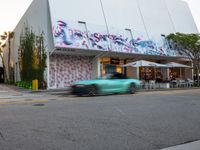 a car is passing a large building with graffiti on it's side, on the street