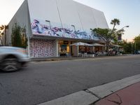 a car is passing a large building with graffiti on it's side, on the street