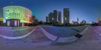 a skateboard park with buildings and a blue sky in the background at night in the distance