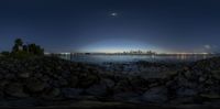 a full moon is rising over the skyline of a city as seen from a rocky shore