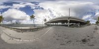 this is a fish eye photo of a bridge over the ocean with palm trees around it