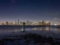 a very long beach on the waterfront with lights shining over the skyline of city in the background