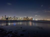 a very long beach on the waterfront with lights shining over the skyline of city in the background