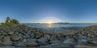 a view from some rocks over a large body of water and the sun setting behind the city skyline