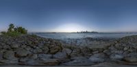 a large body of water next to a rocky beach and an island with a very tall skyscraper in the distance