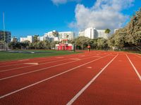 the run track has lanes for racing on it and trees in the background with high rise residential buildings in the distance