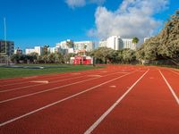 the run track has lanes for racing on it and trees in the background with high rise residential buildings in the distance