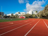 the run track has lanes for racing on it and trees in the background with high rise residential buildings in the distance