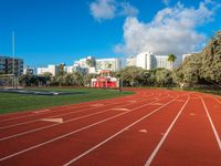 the run track has lanes for racing on it and trees in the background with high rise residential buildings in the distance