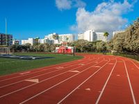 the run track has lanes for racing on it and trees in the background with high rise residential buildings in the distance