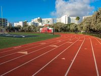 the run track has lanes for racing on it and trees in the background with high rise residential buildings in the distance