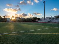 an empty soccer field with the sun setting behind it in an urban setting, on a cloudy day