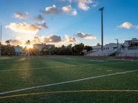 an empty soccer field with the sun setting behind it in an urban setting, on a cloudy day