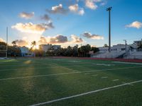 an empty soccer field with the sun setting behind it in an urban setting, on a cloudy day