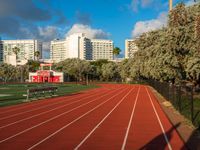 a running track with grass in front and large buildings in the background behind it on a sunny day