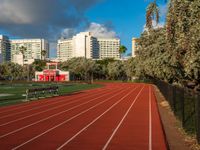 a running track with grass in front and large buildings in the background behind it on a sunny day