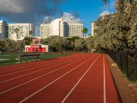 a running track with grass in front and large buildings in the background behind it on a sunny day