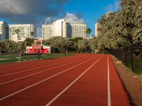 a running track with grass in front and large buildings in the background behind it on a sunny day