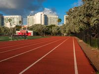 a running track with grass in front and large buildings in the background behind it on a sunny day