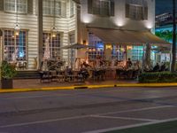 an outside cafe on a corner near the street at night with people sitting outside at tables