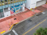 the street is painted pink and has a mural on it behind a small shop on the corner