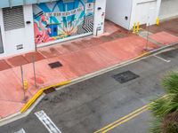 the street is painted pink and has a mural on it behind a small shop on the corner