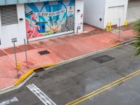 the street is painted pink and has a mural on it behind a small shop on the corner