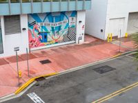 the street is painted pink and has a mural on it behind a small shop on the corner