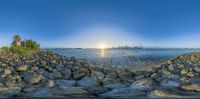 a panoramic photo of a beautiful sunrise over the water, with rocks and trees