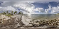 a panoramic view of the water and sand on a beach with rocks, grass, and coconut trees