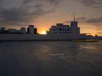 sunset over a parking lot with buildings in the background and cloudy sky above them,