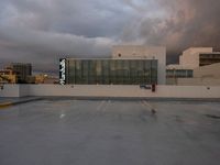 an empty parking lot with cars parked in it and sky and storm clouds overhead the place