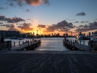 a pier with boats docked at sunset next to a city skyline and body of water