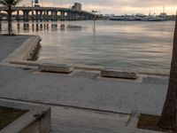 a man walking along a boardwalk at sunset with the water flowing under him and city in the background