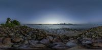 the sun sets behind the city skyline on an ocean shore as seen from a rock outcropping