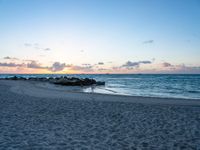 a lone bench sits on the beach as the sun sets behind clouds and water in the background